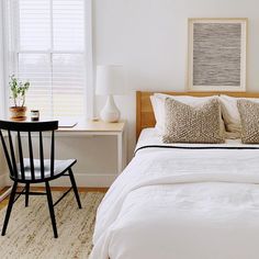 a bed with white sheets and pillows in a bedroom next to a table with a lamp on it