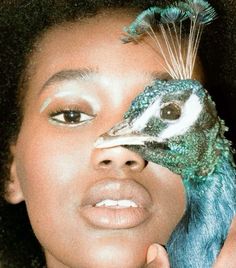 a woman holding a bird in front of her face with feathers on it's head