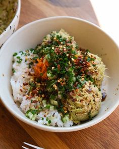 a bowl filled with rice and veggies next to a fork on a wooden table