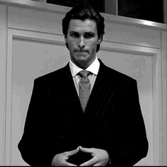 a man wearing a suit and tie standing in front of a door with his hands folded