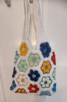 a crocheted purse hanging from a hook on a white door with colorful flowers