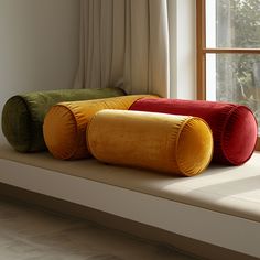 three different colored pillows sitting on top of a window sill