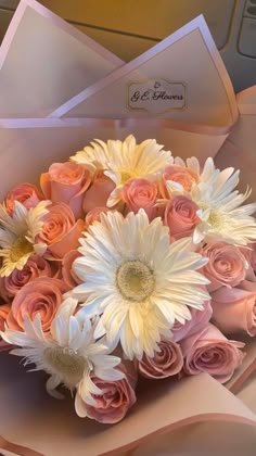 a bouquet of pink roses and white daisies in a paper box with envelopes