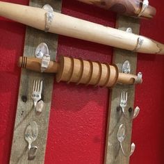 forks, knives and spoons are attached to wooden pegs on a red wall