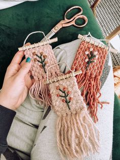 someone is holding two pieces of weaving on a green cushion with scissors and yarn in the background