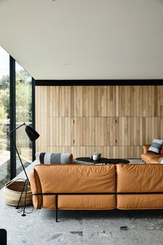 an orange leather couch sitting in front of a wooden paneled wall next to a floor lamp