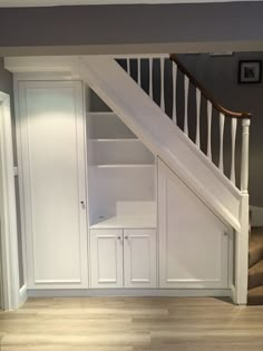 an empty room with white cupboards under the stair case and wooden flooring in front of it