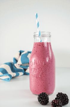 a pink smoothie in a mason jar with blackberries and a blue striped straw