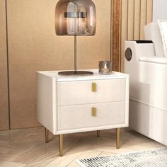 a white nightstand with a lamp on top of it next to a bed in a room