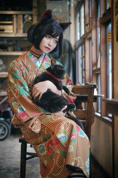 a woman sitting on a chair holding a cat in her lap and wearing a kimono