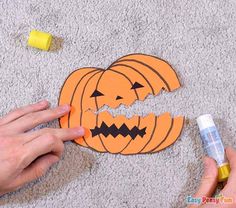 someone is cutting out a pumpkin cutout with glue on the floor next to it