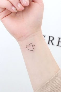 a woman's wrist with a small heart and arrow tattoo on her left arm