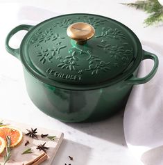 a green casserole on a white table with orange slices and spices next to it