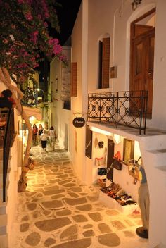 an alley way with people walking down it at night, lined with shops and restaurants