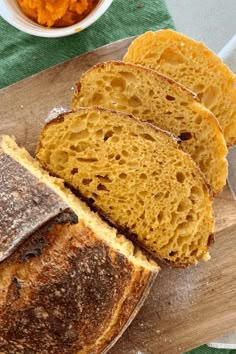 slices of bread sitting on top of a cutting board next to a bowl of carrots