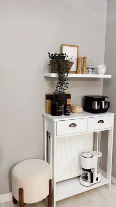 there is a small white table with a plant on it and a stool in front of it