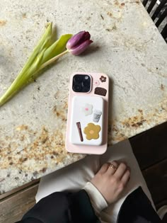 a person sitting at a table with a cell phone case on their lap, next to a flower