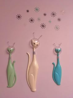 three cat shaped objects on a pink wall with snowflakes in the back ground