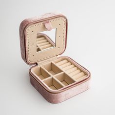 an open pink case with compartments for jewelry on a white surface, showing the inside