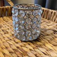 a glass candle holder sitting on top of a wicker table next to a basket