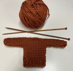 two skeins of yarn and knitting needles are on the table next to an orange knitted sweater