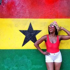 a woman standing in front of a wall with a flag painted on it and her hands behind her head