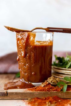 a glass filled with sauce sitting on top of a wooden cutting board next to plates