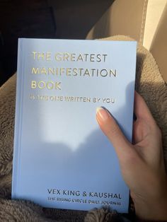 a person holding up a book in their hand with the title, the greatest maniestation book on it