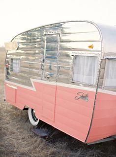 an old pink and silver trailer parked in a field