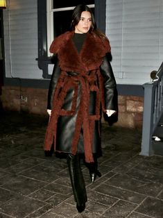 a woman is walking down the street wearing a fur coat and black leather pants with her hands in her pockets