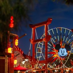 an amusement park at night with lights on the ferris wheel and mickey mouse sign in front