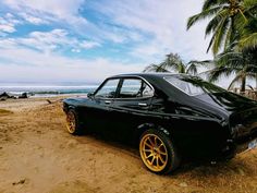 an old black car parked on the beach next to palm trees and ocean in the background