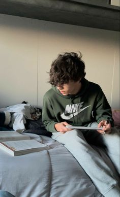 a young man sitting on top of a bed next to a white book and headphones