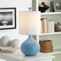 a blue table lamp sitting on top of a white desk next to a book shelf