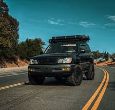 a black suv driving down the road with its lights on and an off - road vehicle behind it