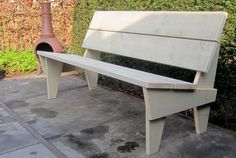 a white bench sitting on top of a cement ground next to a bush and fire hydrant