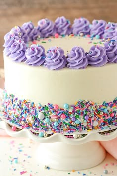 a white cake with purple frosting and sprinkles on the top layer