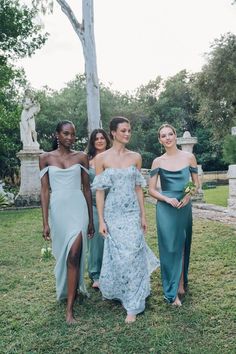 three women in dresses standing next to each other on the grass with trees and statues behind them