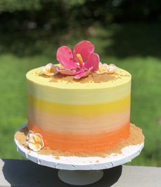 a multicolored cake sitting on top of a wooden table next to a green field