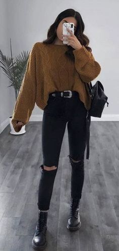 a woman taking a selfie while wearing black ripped jeans and a brown turtle neck sweater