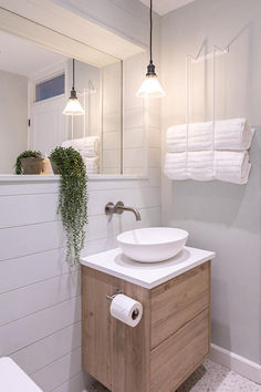 Minimalist bathroom featuring a clear glass pendant light, white vessel sink on a wood vanity, white paneled walls, and accents of greenery and neatly stacked towels. Interior Themes, Casting Shadows, Glass Lights, Bathroom Pendant, Vintage Bulbs, Black Ceiling, Light Crafts, Wood Vanity, Ceiling Rose