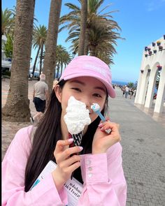 a woman holding an ice cream cone in front of her face while wearing a pink hat