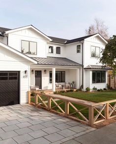 a large white house with two garages and a wooden fence in front of it