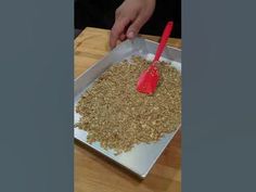 a person scooping oatmeal from a pan onto a wooden table with a red spatula