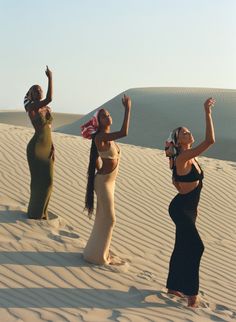 three beautiful women standing in the sand with their arms up and one holding a scarf