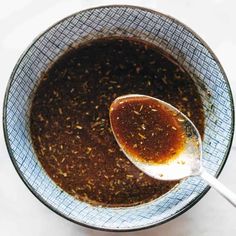 a spoon in a bowl filled with brown liquid and seasoning flakes on the side