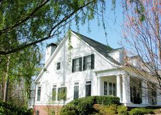 a large white house with black shutters on the front and side windows, surrounded by trees