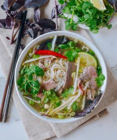 a bowl of soup with noodles, meat and vegetables on a napkin next to chopsticks