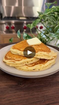 a white plate topped with pancakes and butter on top of a wooden table next to a potted plant