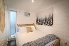 a white bed sitting in a bedroom next to a wall mounted air conditioner and window